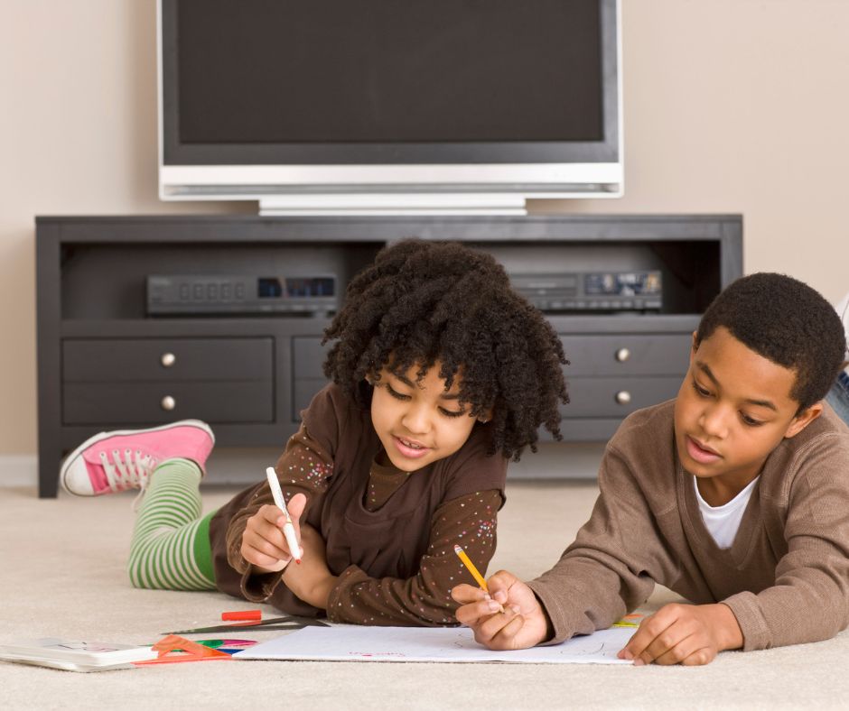 A brother and sister are sitting on the living room floor, coloring together. Coloring books can help children learn about colors, shapes, and numbers, while also improving their concentration and hand-eye coordination.