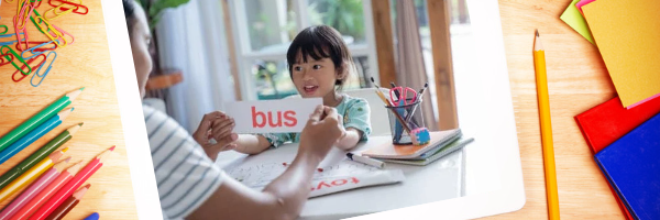 A father and daughter sitting together, with the daughter reading a sign that says bus. The father is helping her learn to decode cvc words.