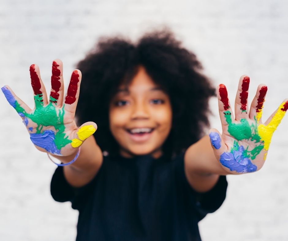 A young girl with outstretched hands covered in paint.